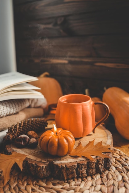 Burning candle pumpkin and a cup of tea on the background of a stack of sweaters autumn composition