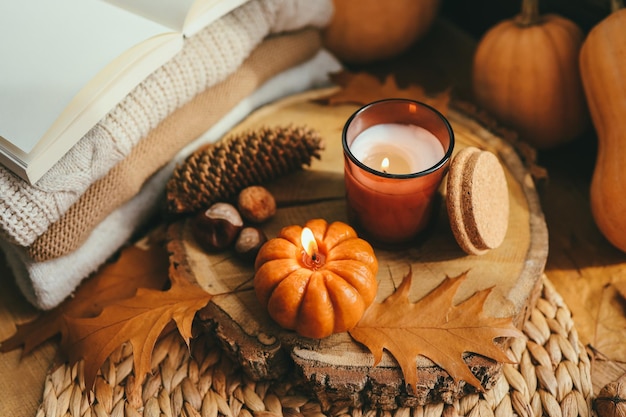 Burning candle pumpkin and a cup of tea on the background of a stack of sweaters autumn composition