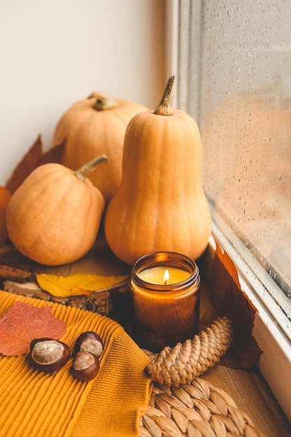 Photo burning candle and pumpkins on the windowsill rain outside the window autumn atmosphere