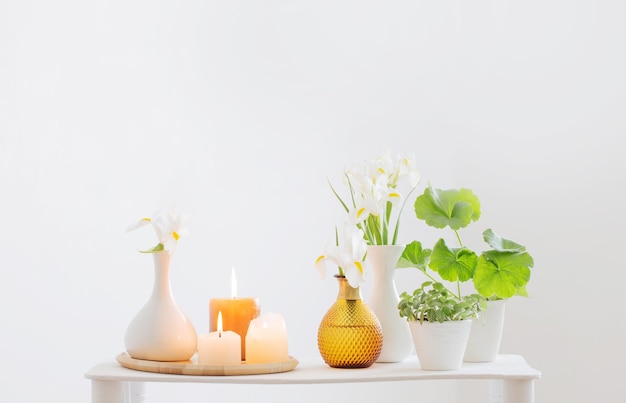 Burning candles and spring flowers on wooden shelf in white interior