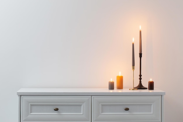 Burning candles on white wooden shelf in white interior