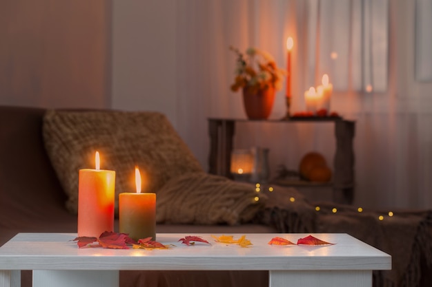 Burning candles with autumn decor on white table at home