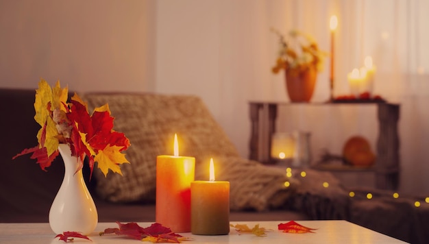 burning candles with autumn decor on white table at home