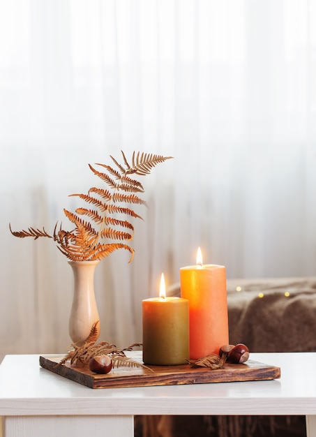 Burning candles with autumn decor on white table at home