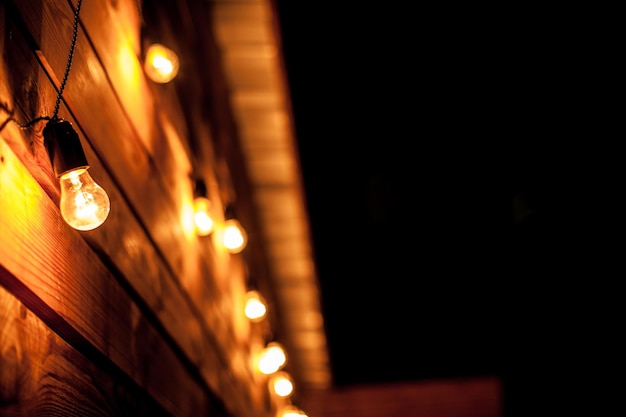 Burning garlands garland on a wooden background. Light bulbs on wooden background. Evening Wooden Stage In The Garden With Lamps For Parties Or Wedding