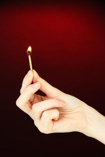 Burning match in female hand on dark red background