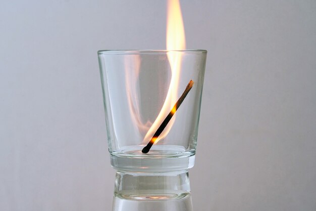 Burning match in a transparent glass on a light background