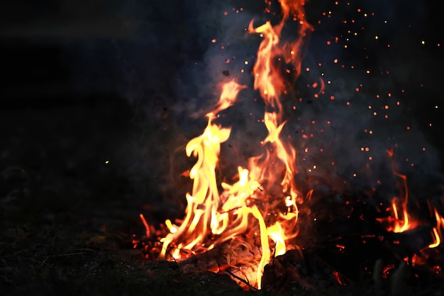 Burning red hot sparks fly from big fire. Burning coals, flaming particles flying off against black background.