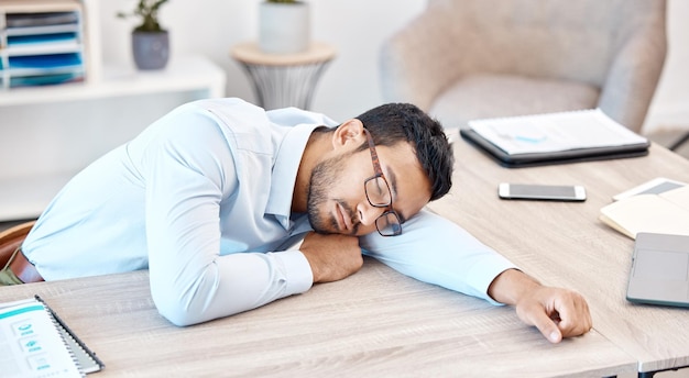 Burnout sleeping and tired with an overworked business man asleep at his desk in the office Exhausted fatigue and dreaming with a young male employee napping on a table at work after working late