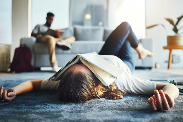 Burnout student and tired woman with book on her face for knowledge exhaustion and fatigue College university and problem with a female lying on the floor covered in a notebook for studying