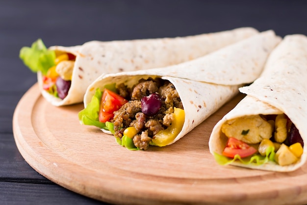 Burrito with beef, chicken, lime, pepper and vegetables, on a wooden board