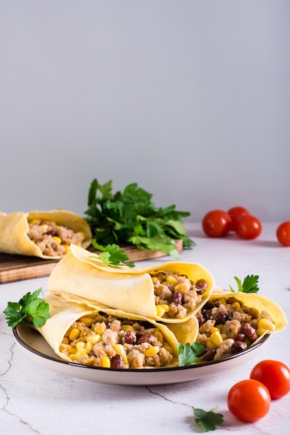 Burrito with minced meat corn beans and tomatoes in corn tortillas on a plate Vertical view