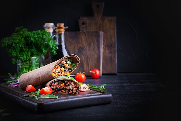 Burritos wraps with beef and vegetables on  dark wooden background. Beef burrito, mexican food.