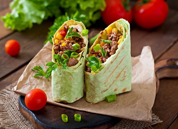 Photo burritos wraps with minced beef and vegetables on a wooden background