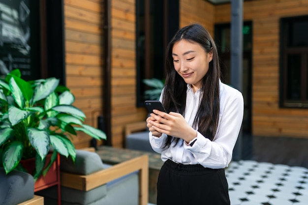 Business asian woman stands in the corridor and looks into a mobile phone decides matters