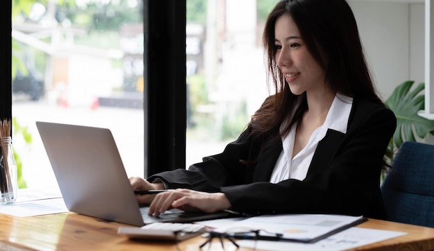 Business asian woman using laptop for do math finance on wooden desk in office, tax, accounting, financial concept