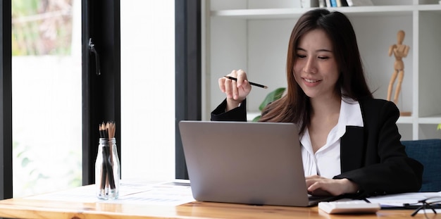 Business asian woman using laptop for do math finance on wooden desk in office, tax, accounting, financial concept