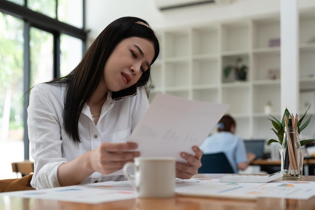 Business asian woman working with paperwork calculator at office while talking on phone