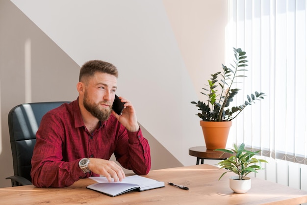 Business bearded man is talking on phone and plans to meet daily and write