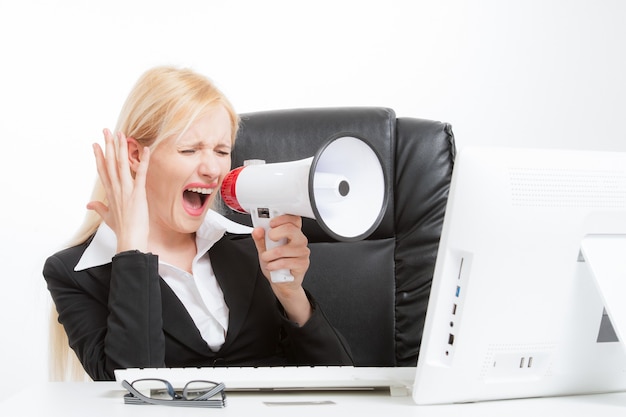 Business blonde woman sitting behind the desk and screaming through a megaphone