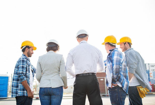 business, building, teamwork and people concept - group of builders and architects in hardhats with blueprint on construction site