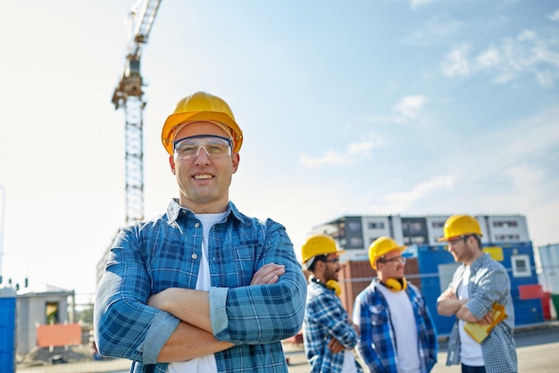 business, building, teamwork and people concept - group of smiling builders in hardhats at construction site