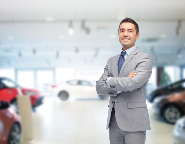 business, car sale, consumerism and people concept - happy man over auto show or salon background