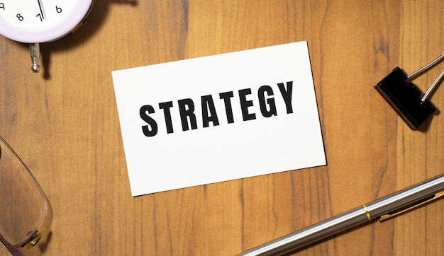 A business card with the text STRATEGY lies on a wooden office table among office supplies. Business concept.