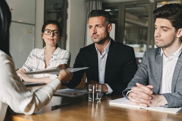 Business, career and placement concept - board of directors sitting at table in office, and examining resume of female worker during meeting