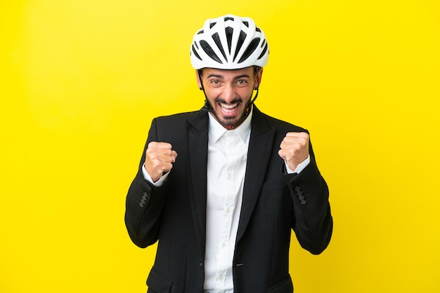 Business caucasian man with a bike helmet isolated on yellow background celebrating a victory in winner position