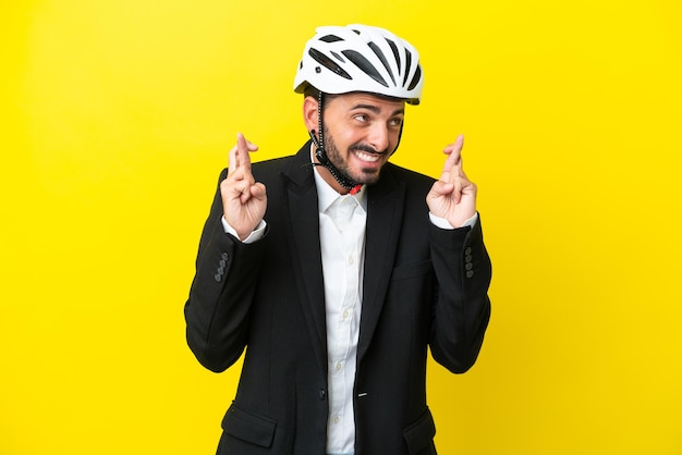 Business caucasian man with a bike helmet isolated on yellow background with fingers crossing