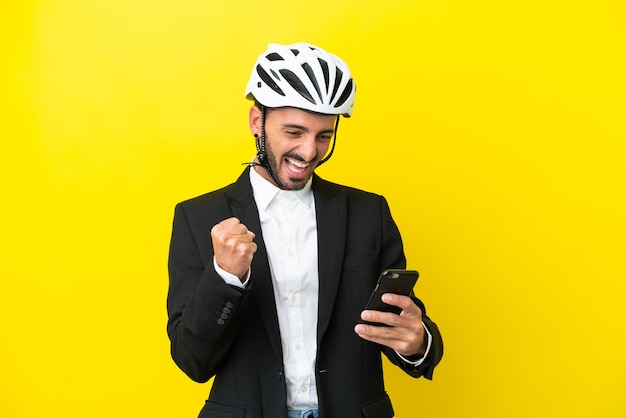 Business caucasian man with a bike helmet isolated on yellow background with phone in victory position