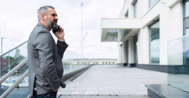 Business caucasian senior businessman speaks by mobile phone at the entrance to the business center