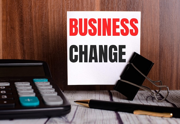 BUSINESS CHANGE is written on a white card on a wooden surface next to a calculator and pen