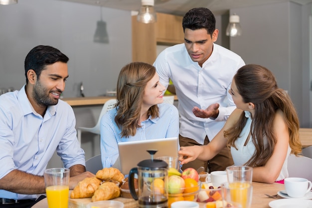 Business colleagues discussing over digital tablet while having breakfast