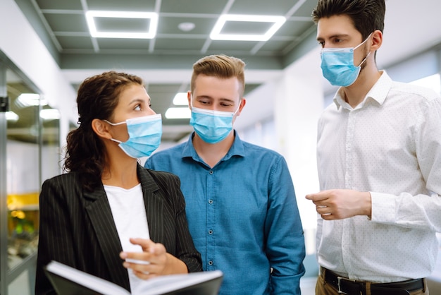 Business colleagues in protective face masks in modern office discussing together work issues.