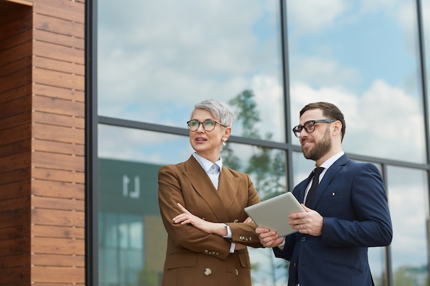 Business colleagues talking to each other while standing outdoors and using digital tablet