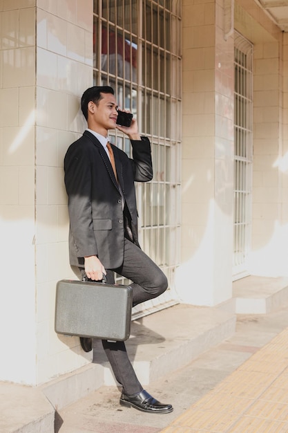 Business communications. Happy young Asian man in formal wear talking on the phone and smiling while