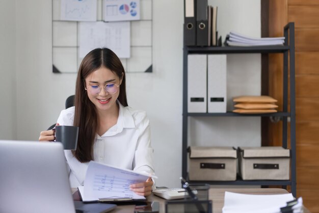 Business concept Businesswoman is reading financial document and drinking coffee in modern office