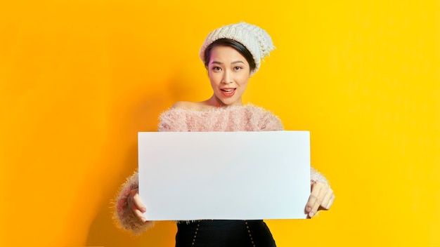 Business Concept Close up Portrait young beautiful attractive Asian smiling showing plain white blank sign Yellow Background