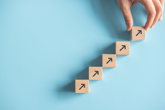 Photo business concept growth success process, close up woman hand arranging wood block stacking as step stair on paper blue background, copy space.