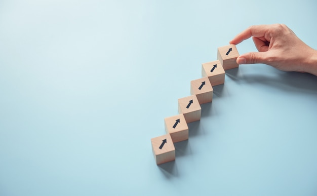 Business concept growth success process, Close up Woman hand arranging wood block stacking as step stair on paper blue background, copy space.