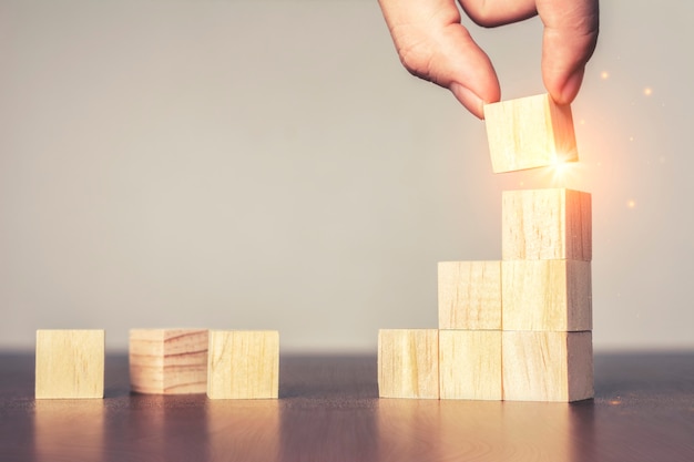 Business concept growth success process and Hand arranging wood block stacking as step stair on table.