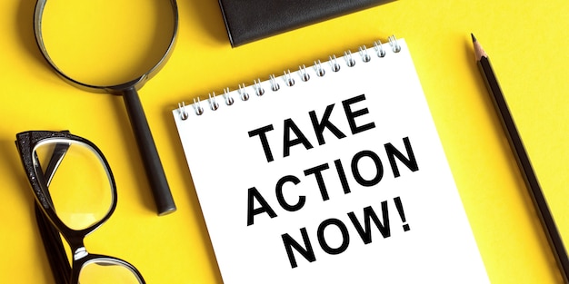 Business concept image of a office table with glasses, magnifier, pencil and notebook and write motivational quotes Take Action Now