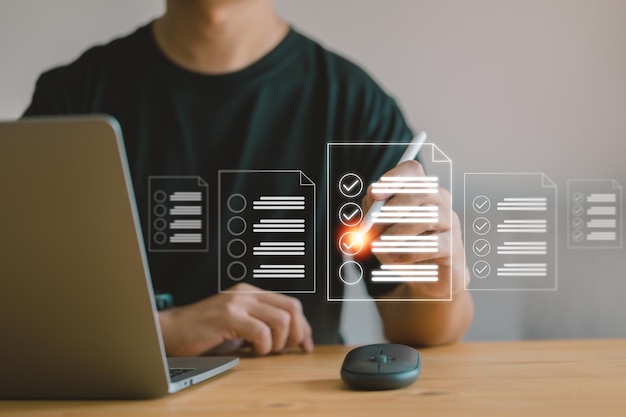 Business concept and smart checklist on a virtual screen In a modern office a man uses a pen to make notes about exploring the topics on the digital form check document sheet and a laptop to work