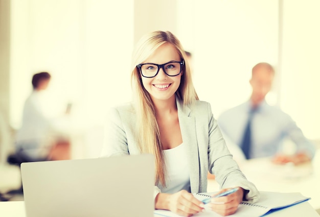 business concept - smiling woman with laptop, documents and pen in office