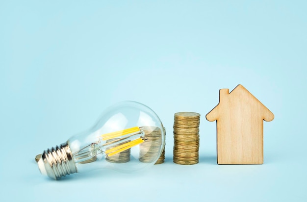 Business concept Wooden house lamp and coins on a blue background Communal payments Electricity