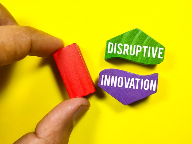 Business conceptText DISRUPTIVE INNOVATION with hand holding colored wooden block on a yellow background