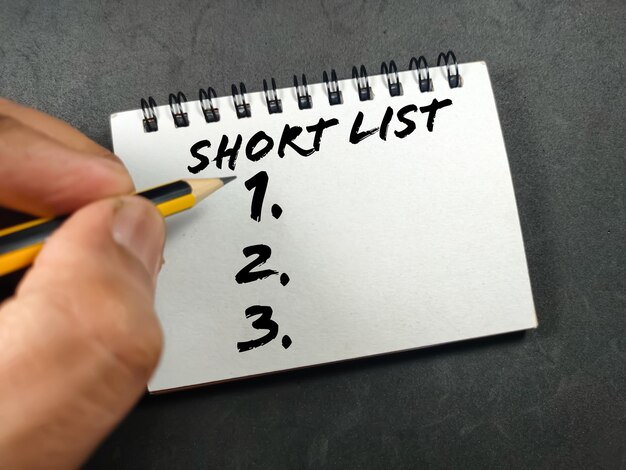 Business conceptText SHOT LIST with hand holding pencil on notebook with black background