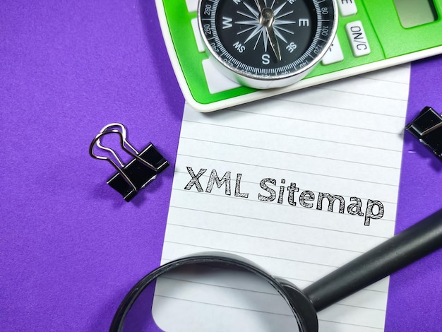 Business conceptText XML Sitemap writing on notepaper with magnifying glasscompasscalculator and paper clips on purple background